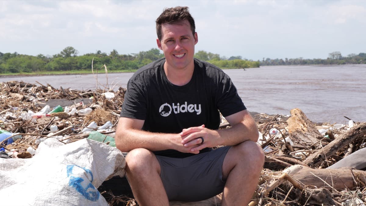 Tidey Ocean founder at a polluted riverbank full of plastic waste